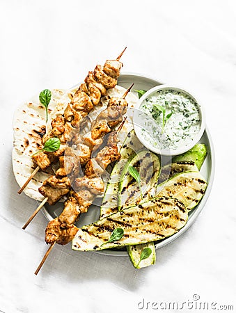 Chicken skewers souvlaki, grilled zucchini, tortillas and tzadziki sauce - delicious greek style lunch on a light background, top Stock Photo