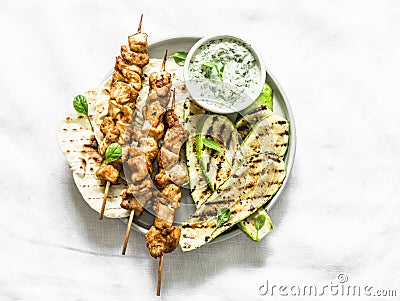 Chicken skewers souvlaki, grilled zucchini, tortillas and tzadziki sauce - delicious greek style lunch on a light background, top Stock Photo