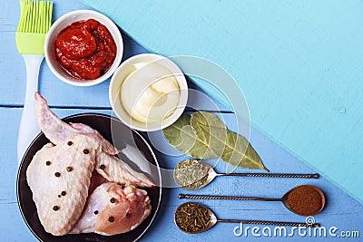 Chicken wings with black pepper, mayonnaise and tomato paste for rustic kitchen. Spoons with spices and bay leaves with culinary b Stock Photo