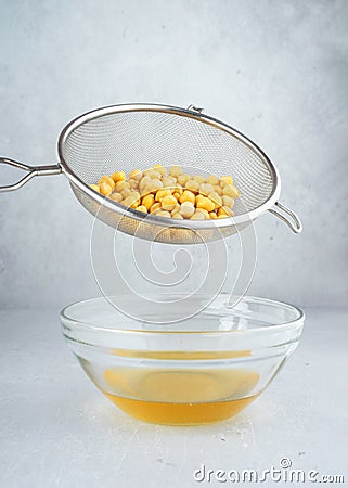 Chickpea water aquafaba. Egg replacement. Vegan concept. Metal sieve draining aquafaba chickpea water into glass bowl. on a gray Stock Photo