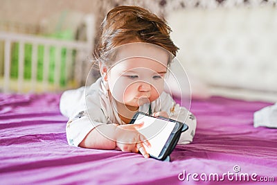 Child addiction to phones. radiation from the phone to the child. A little boy 0-1 years old with a smartphone in his hands looks Stock Photo