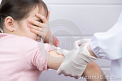 The child is afraid and covers his face with his hand, the doctor wants to vaccinate him Stock Photo
