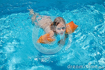 Child with armbands swimming in transparent blue water of pool Stock Photo