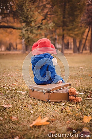 A child in a blue coat and a red hat is sitting on a suitcase Stock Photo