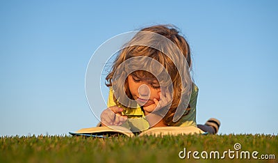 Child boy with a book in the garden. Kid is readding a book playing outdoors in summer day. Kids imagination, innovation Stock Photo