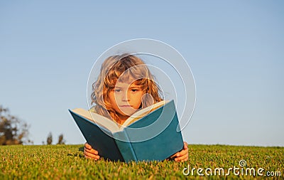 Child boy with a book in the garden. Kids success, successful leader concept. Kid is readding a book playing outdoors in Stock Photo