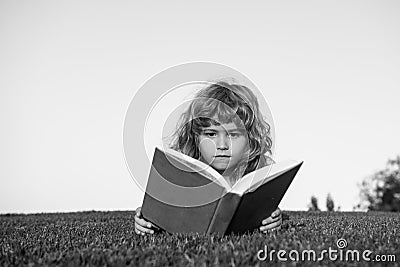 Child boy with a book in the garden. Kids success, successful leader concept. Kid is readding a book playing outdoors in Stock Photo