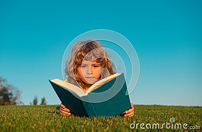 Child boy with a book in the garden. Kids success, successful leader concept. Kid is readding a book playing outdoors in Stock Photo