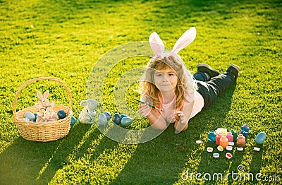 Child boy with easter eggs and bunny ears laying on grass. Easter kids with bunny ears and on grass background. Stock Photo