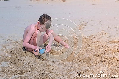 Child boy playing on sand beach digging shovel and trying to build sand tower. Stock Photo
