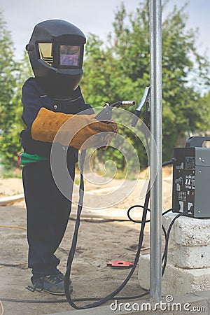 A child, a boy pretends to weld a fence. Welder`s costume, gloves, mask. Stock Photo