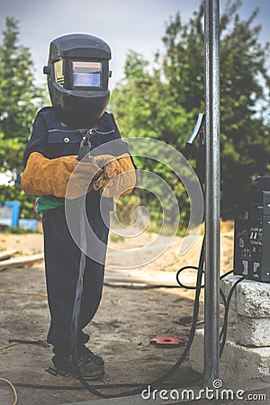 A child, a boy pretends to weld a fence. Welder`s costume, gloves, mask. Stock Photo