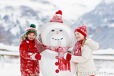 Child building snowman. Kids build snow man. Boy and girl playing outdoors on snowy winter day. Outdoor family fun on Christmas Stock Photo