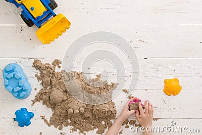 A child builds figures from kinetic sand. Top view on colorful sand molds and other toys on a white wooden table. Early Stock Photo