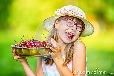 Child with cherries. Little girl with fresh cherries. Young cute caucasian blond girl wearing teeth braces and glasses. Stock Photo