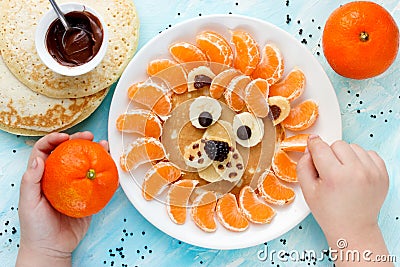 Child cooking and eating funny breakfast lion pancake with tangerines Stock Photo