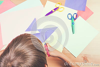 Child cutting colored paper with scissors at the table Stock Photo