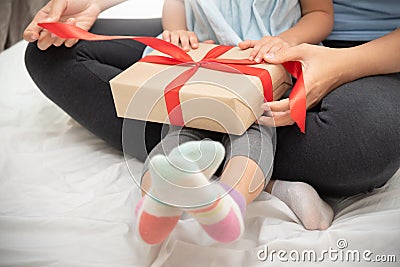 Child daughter unwrapping gift box with her mom Stock Photo