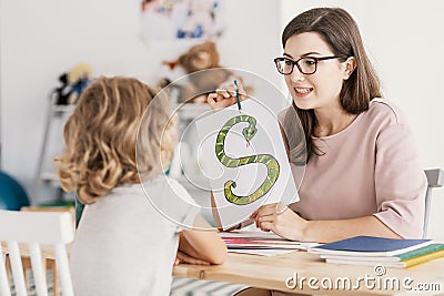 A child with development problems with a professional speech therapist during a meeting. Tutor holding a prop poster of a snake as Stock Photo