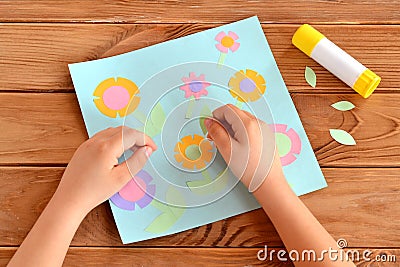 Child doing a card with flowers. Child holds a paper leaf in his hands and sticks it. Glue, greeting card on a wooden table Stock Photo