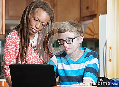 Child doing homework with foster parent in kitchen Stock Photo