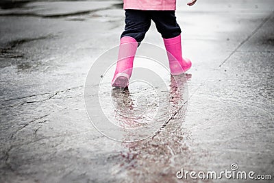 Child dressed in pink clothes jumping in puddles Stock Photo