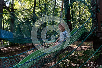 Child enjoying a playful adventure on a slide in a treehouse playground surrounded by greenery and safety netting. Stock Photo