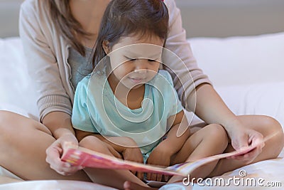 A child enjoying reading a book in bed with her mother Stock Photo