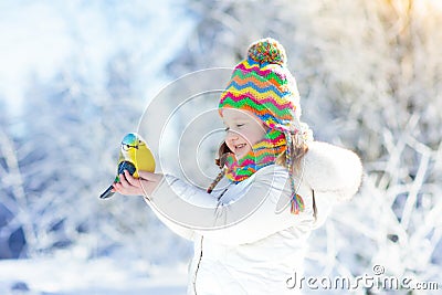 Child feeding bird in winter park. Kids play in snow. Nature and Stock Photo