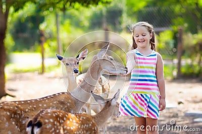 Child feeding wild deer at zoo. Kids feed animals. Stock Photo