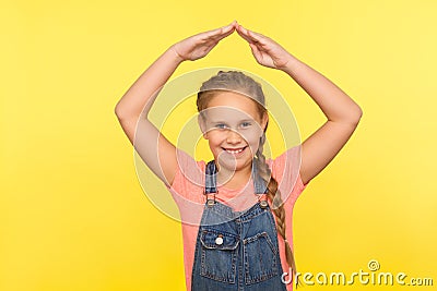 Child feel safe. Portrait of happy little girl with braid in denim overalls standing under house roof gesture Stock Photo
