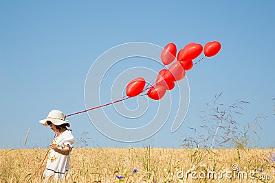 Child with flying red heart balloons on the blue sky background. Stock Photo