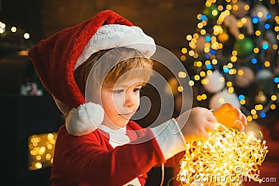 Child with garland lights at Christmas tree and fireplace on Xmas eve. It is miracle. Family with kids celebrating Stock Photo