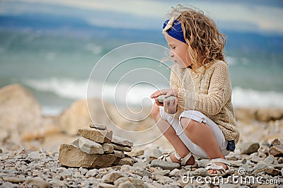 Child girl building stone tower on the beach in summer day Stock Photo