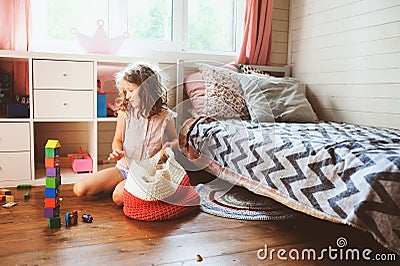 Child girl cleaning her room and organize wooden toys into knitted storage bag Stock Photo