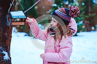 Child girl feeding birds in winter. Bird feeder in snowy garden, helping birds during cold season Stock Photo