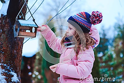 child girl feeding birds in winter. Bird feeder in snowy garden, helping birds during cold season Stock Photo