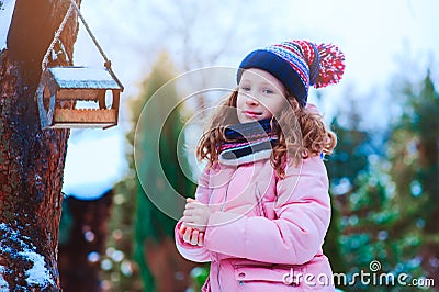 Child girl feeding birds in winter. Bird feeder in snowy garden, helping birds during cold season Stock Photo