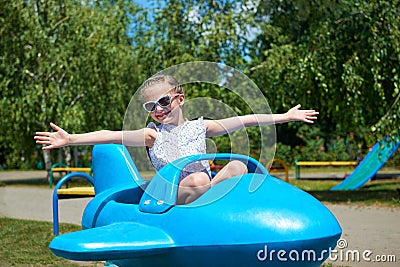 Child girl fly on blue plane attraction in city park, happy childhood, summer vacation concept Stock Photo