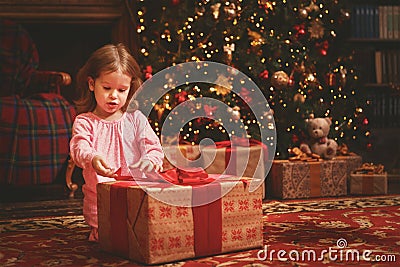 Child girl in a nightgown in Christmas night opening gifts at Ch Stock Photo