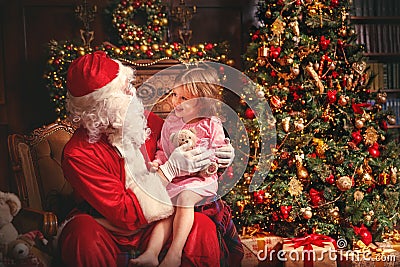 child girl in nightgown sitting on lap of Santa Claus around Christmas tree Stock Photo