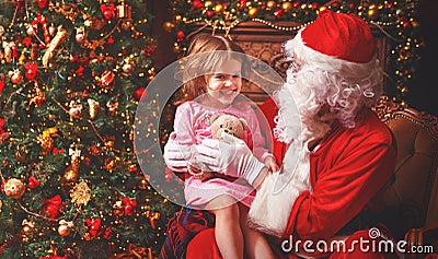 child girl in nightgown sitting on lap of Santa Claus around Christmas tree Stock Photo