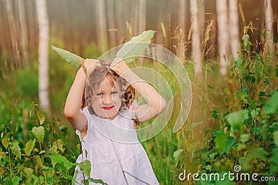 Child girl playing with green leaves in summer forest Stock Photo