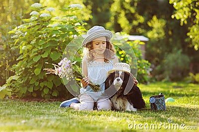 child girl playing with her spaniel dog in summer garden, both wearing funny gardener hats Stock Photo