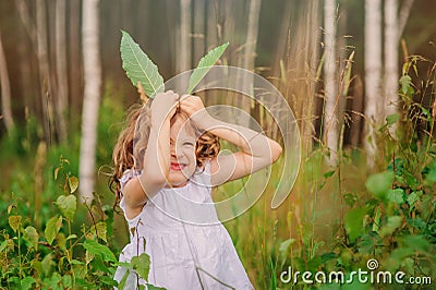Child girl playing with leaves in summer forest with birch trees. Nature exploration with kids. Stock Photo