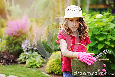 Child girl playing little gardener and helping in summer garden, wearing hat and gloves Stock Photo