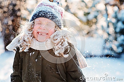 Child girl playing with snow in winter garden or forest, making snowballs and blowing snowflakes Stock Photo