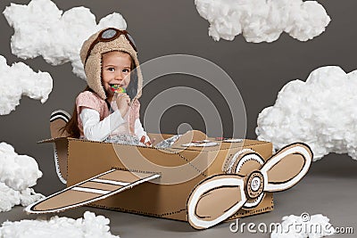 The child girl plays in an airplane made of cardboard box and dreams of becoming a pilot, clouds of cotton wool on a gray backgrou Stock Photo