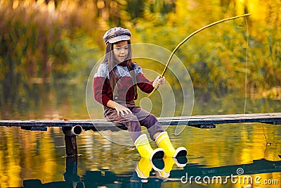 Child girl sits on wooden fishing bridge and catches fish in autumn. Stock Photo