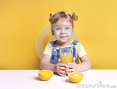 Child girl at table with glass of orange juice.Fresh fruits,vitamin nutrition. Caucasian kid portrait with beverage on yellow Stock Photo